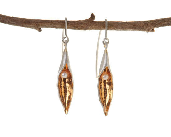 Medium silver pod earrings with gold inside and a white pearl in each. The earring hooks hang from a twig