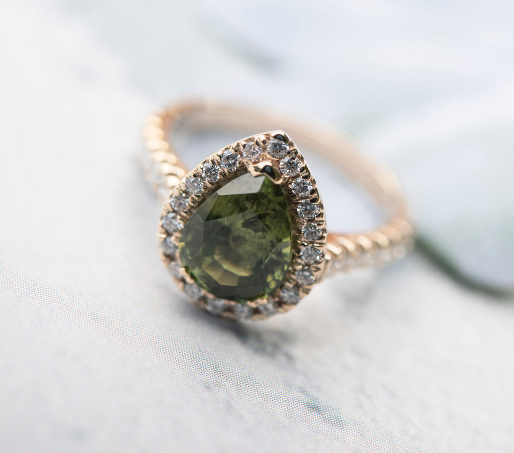 Large pear shaped green sapphire set in a diamond halo head on a gold ring