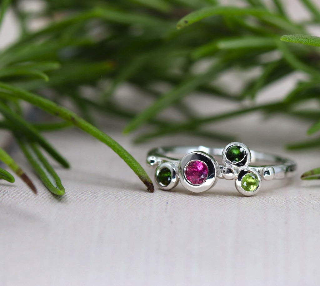 silver ring with pink and green gemstones in front of a sprig of rosemary