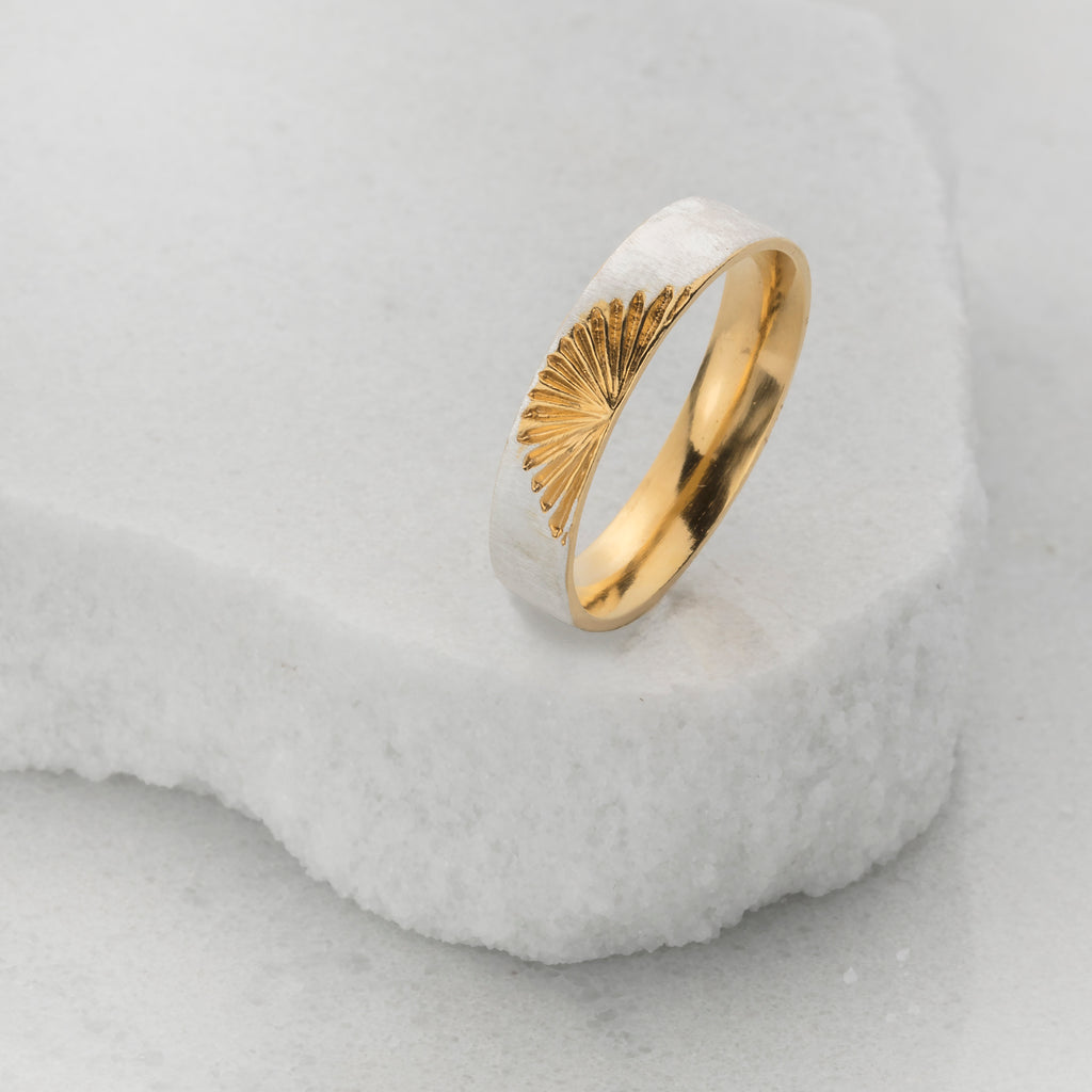 silver ring with golden sunset and gold inside ring sitting on white rock