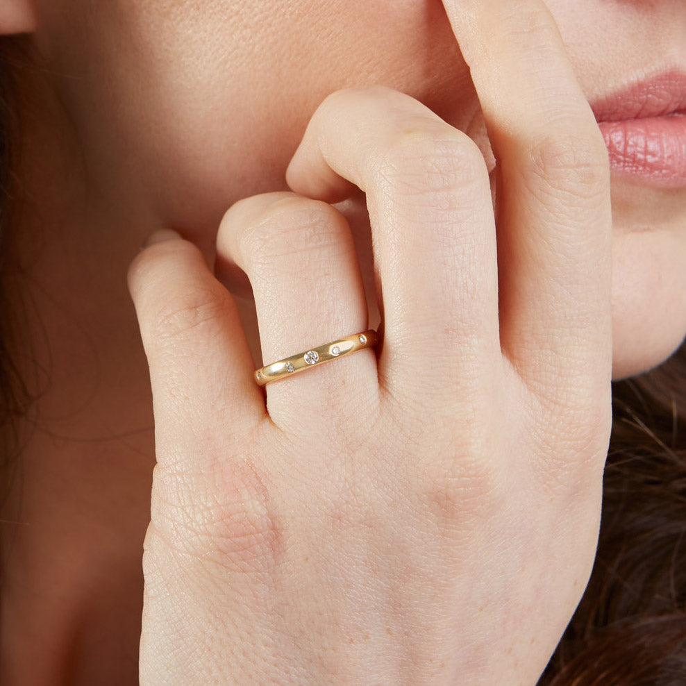 Woman with hand to her face. She is wearing a yellow gold and diamond wedding ring on her ring finger