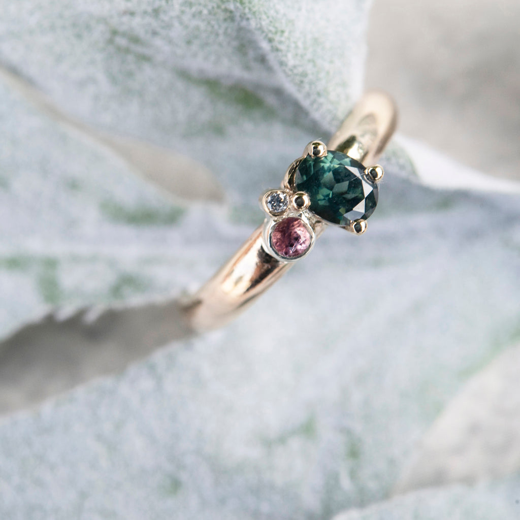 gold ring with teal, pink and white gemstones sitting on a leaf